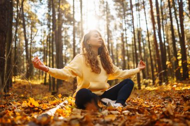 Spor giyim sektöründe aktif bir kadın sonbahar ormanında düşen yapraklar üzerinde yoga egzersizleri yapıyor, zen, meditasyon, rahatlama yapıyor. Rahatlama, özgürlük kavramı..