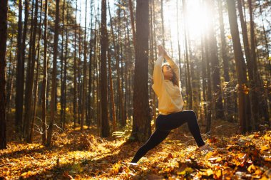 Spor giyim sektöründe aktif bir kadın sonbahar ormanında düşen yapraklar üzerinde yoga egzersizleri yapıyor, zen, meditasyon, rahatlama yapıyor. Rahatlama, özgürlük kavramı..