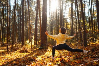 Spor giyim sektöründe aktif bir kadın sonbahar ormanında düşen yapraklar üzerinde yoga egzersizleri yapıyor, zen, meditasyon, rahatlama yapıyor. Rahatlama, özgürlük kavramı..