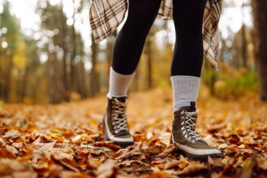 Sonbahar havası. Parktaki sonbahar yaprakları üzerinde yürüyüş botlarıyla kadın bacaklarının yakın çekimi. Doğa konsepti, rahatlama, yürüme.