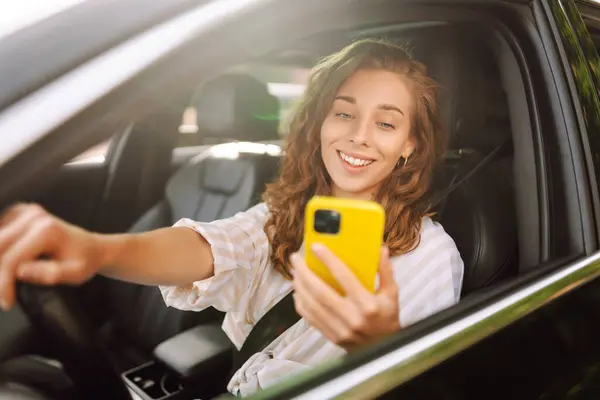Beautiful female driver uses a smartphone in the car. A woman driving a car uses a mobile phone to pay for parking and move around the city.
