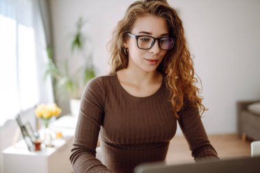 Günlük giysiler içindeki iş kadını dizüstü bilgisayar ve not defteriyle çalışıyor. Genç bir kadın müşterileriyle internet üzerinden görüşüyor, çalışıyor ve modern bir kuna üzerinde otururken ders çalışıyor. Eğitim kavramı, serbest çalışma.