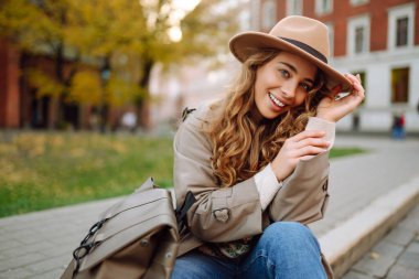 Sıradan kıyafetler ve şapkalı mutlu bir kadın şehir sokaklarında oturmuş mimarinin tadını çıkarıyor, güneşli havanın tadını çıkarıyor. Seyahat, hafta sonu konsepti.