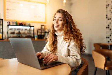 Dizüstü bilgisayarı olan güzel bir kadın rahat bir kafede oturmuş çalışıyor. Çevrimiçi eğitim kavramı, serbest çalışma, teknoloji.