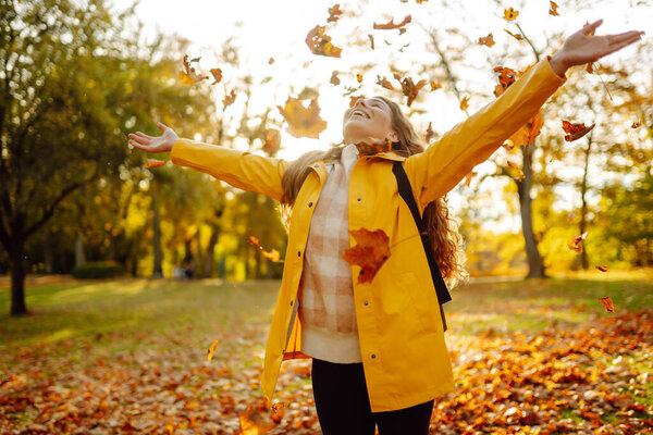Красивая женщина бросает осенние желтые листья. Счастливая туристка, развлекающаяся и наслаждающаяся природой в осеннем парке. Концепция релаксации, веселья, сплоченности с природой.