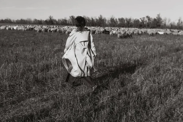 Tarlada, kuru otların arasında paltolu şık bir kadın, doğanın tadını çıkarıyor. Siyah beyaz fotoğraf. Doğa, moda, özgürlük kavramı. Yaşam biçimi.