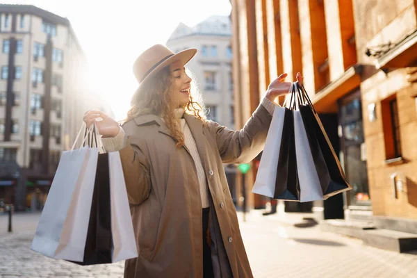 Gün batımında elinde hediyelerle şehir sokaklarında mutlu bir kadın. Çevrimiçi alışveriş konsepti, alışveriş, indirim. Tüketim kavramı.