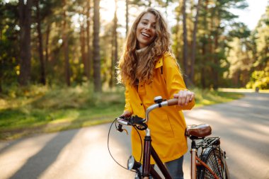 Sonbahar parkında bisiklet süren gülümseyen bir kadın. Güzel bayan turist bisiklet sürüyor, güneşli sıcak havanın tadını çıkarıyor. Yaşam tarzı, hafta sonu konsepti. 