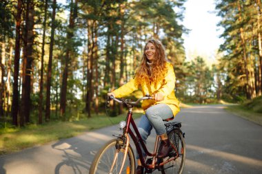 Sonbahar parkında bisiklet süren gülümseyen bir kadın. Güzel bayan turist bisiklet sürüyor, güneşli sıcak havanın tadını çıkarıyor. Yaşam tarzı, hafta sonu konsepti. 