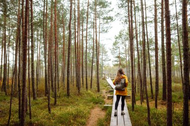 Sarı paltolu mutlu kadın, çevresindeki yeşil ve doğal ormanın tadını çıkarıyor. Sırt çantalı bir turist ormanın çalılıklarında yeni yerler keşfediyor..