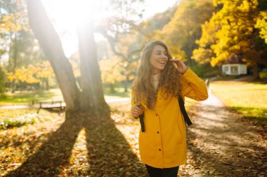 Sonbahar ormanında yürüyüş. Parlak ceketli gülümseyen bir turist güneşli bir havada sonbahar parkında yürür. Seyahat, macera ya da hafta sonu konsepti.