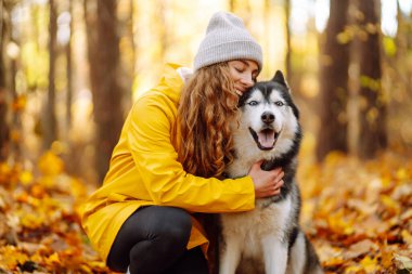 Sarı montlu güzel genç bir kadın güz parkında evcil köpeğiyle yürüyor. Bir evcil hayvan sahibi köpeğiyle vakit geçirir. Eğlence anlayışı, eğlence.
