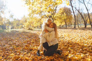 Merhaba Autumn. Gülümseyen anne ve kız, sonbahar parkında sarı yapraklarla eğleniyorlar. Aile yürüyüşü ve birlikte vakit geçirmeyi seviyor..