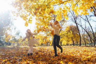 Merhaba Autumn. Gülümseyen anne ve kız, sonbahar parkında sarı yapraklarla eğleniyorlar. Aile yürüyüşü ve birlikte vakit geçirmeyi seviyor..
