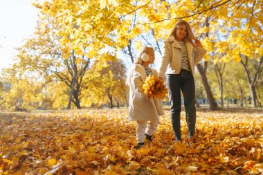 Merhaba Autumn. Gülümseyen anne ve kız, sonbahar parkında sarı yapraklarla eğleniyorlar. Aile yürüyüşü ve birlikte vakit geçirmeyi seviyor..
