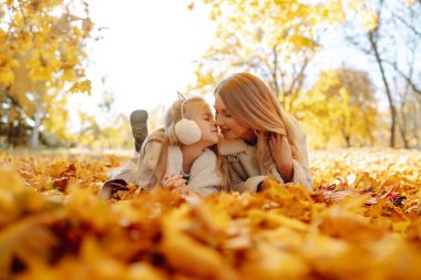 Merhaba Autumn. Gülümseyen anne ve kız, sonbahar parkında sarı yapraklarla eğleniyorlar. Aile yürüyüşü ve birlikte vakit geçirmeyi seviyor..
