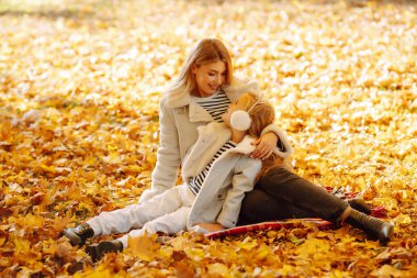 Merhaba Autumn. Gülümseyen anne ve kız, sonbahar parkında sarı yapraklarla eğleniyorlar. Aile yürüyüşü ve birlikte vakit geçirmeyi seviyor..