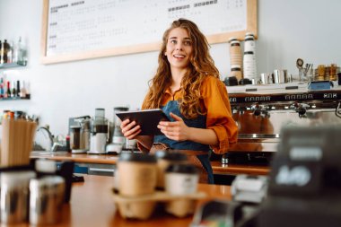 Kadın barmen kahve dükkanında tezgahın arkasında beklerken tabletten sipariş alır. İş, teknoloji kavramı. Paket yemek..