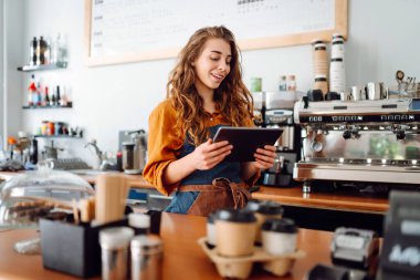Kadın barmen kahve dükkanında tezgahın arkasında beklerken tabletten sipariş alır. İş, teknoloji kavramı. Paket yemek..