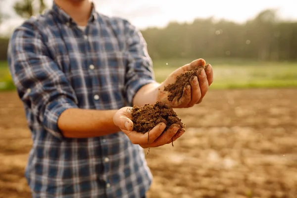 The soil is in the hands of an experienced agronomist. Close-up of a farmer's male hands checking the quality of the soil, the fertility of the land. A worker holds a plowed field of soil.