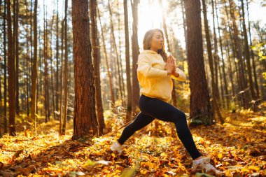 Aktif kadın, sonbahar ormanında sarı yaprakların arasında yoga yapıyor. Zen 'e yakalanıyor. Meditasyon kavramı, rahatlama. Etkin yaşam biçimi.