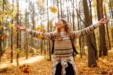 Sırt çantalı genç ve güzel bir turist sonbahar ormanında eğleniyor, yapraklarını döküyor. Kadın ormanda renkli bir patika boyunca yürüyor. Özgürlük, seyahat.