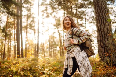Sırt çantalı genç ve güzel bir turist sonbahar ormanında eğleniyor, yapraklarını döküyor. Kadın ormanda renkli bir patika boyunca yürüyor. Özgürlük, seyahat.