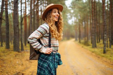 Sırt çantalı şapkalı güzel bir kadın doğa yürüyüşüne çıkmış. Bir gezgin sonbahar ormanında havanın tadını çıkararak yürür. Etkin yaşam biçimi.