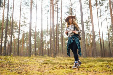 Sırt çantalı şapkalı güzel bir kadın doğa yürüyüşüne çıkmış. Bir gezgin sonbahar ormanında havanın tadını çıkararak yürür. Etkin yaşam biçimi.