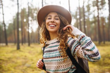 Sırt çantalı şapkalı güzel bir kadın doğa yürüyüşüne çıkmış. Bir gezgin sonbahar ormanında havanın tadını çıkararak yürür. Etkin yaşam biçimi.