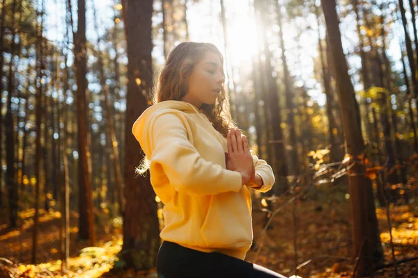 Active woman practices yoga in the autumn forest among yellow fallen leaves, catches zen. Concept of meditation, relaxation. Active lifestyle.