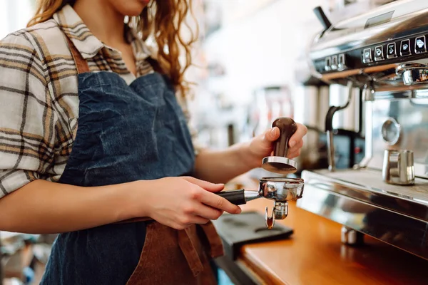 An experienced female bartender prepares a hot drink. A woman in an apron behind the bar prepares fresh coffee. Takeaway food. Professional coffee making.