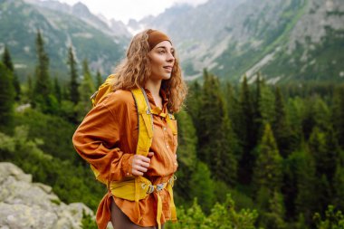 Yürüyüş yolunda parlak bir sırt çantasıyla gülümseyen bir gezgin. Uçurumun tepesinde güzel bir kadın dağ manzarasının tadını çıkarıyor. Etkin yaşam biçimi.