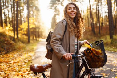 Şık bir süveter ve şapka giyen genç bir kadın bisiklet sürüyor, özgürlüğü hissediyor, ormanda sonbahar havasının tadını çıkarıyor. Açık hava portresi. Etkin yaşam biçimi.