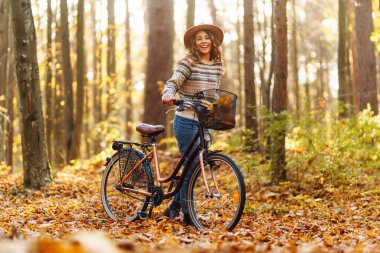 Şapkalı ve kazaklı güzel bir kadın sonbahar parkında bisiklet sürüyor. Aktif turist güneşli havanın tadını çıkarıyor. Hafta sonu konsepti. Etkin yaşam biçimi.