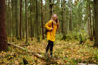 Parlak paltolu kadın gezgin bataklıklar arasında ahşap bir patika boyunca yürüyor. Sırt çantalı bir turist ormanda yürüyor. Seyahat, doğa konsepti..