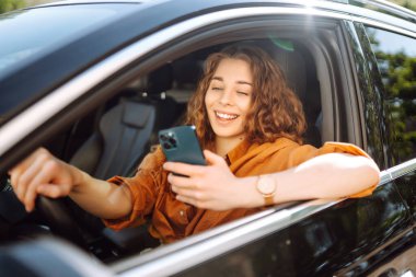 Elinde telefon olan bir arabada güzel bir kadın sürücü. Arabanın sürücüsü bir akıllı telefon kullanıyor. Boş zaman, seyahat, teknoloji, navigasyon.