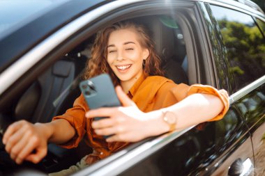 Elinde telefon olan bir arabada güzel bir kadın sürücü. Arabanın sürücüsü bir akıllı telefon kullanıyor. Boş zaman, seyahat, teknoloji, navigasyon.