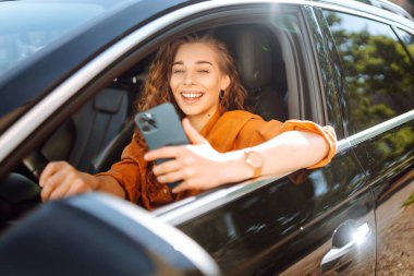 Elinde telefon olan bir arabada güzel bir kadın sürücü. Arabanın sürücüsü bir akıllı telefon kullanıyor. Boş zaman, seyahat, teknoloji, navigasyon.