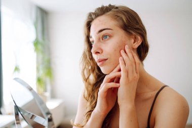 Yüzünde isilik olan tatlı bir kadın küçük bir aynaya bakıyor. Güzel bir kadın sorunlu cildini inceliyor. Doğal güzellik. Kozmetoloji, dikkat.