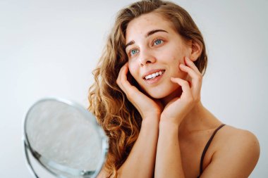 Yüzünde isilik olan tatlı bir kadın küçük bir aynaya bakıyor. Güzel bir kadın sorunlu cildini inceliyor. Doğal güzellik. Kozmetoloji, dikkat.