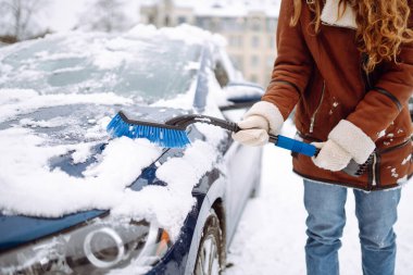 Karı temizleme zamanı! Genç bir kadın bir fırçayla arabadan karı temizliyor. Kış arabası konsepti.