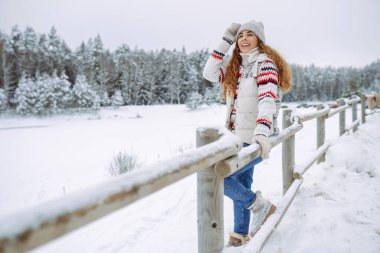 Gülümseyen kadın kış gölünün yanında yürüyor. O, güzel kış havasının tadını çıkarıyor. Kış yürüyüşü kavramı