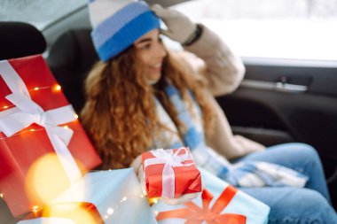 Yeni yıl hediyeleriyle güzel genç bir kadın bir arabanın arka koltuğunda oturuyor. Kış tatili kavramı, hediyeler ve aşk.