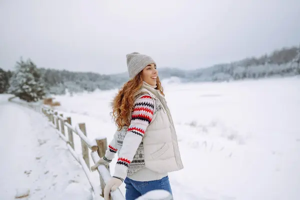 Smiling woman walks near a winter lake. She is enjoying the beautiful winter weather. Winter walk concept