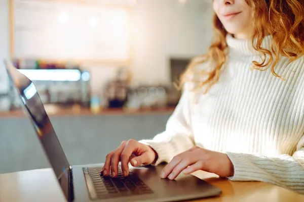 Woman works on a laptop in a cafe. Close-up of hands working on a laptop keyboard.  Freelance, online course. Technology.