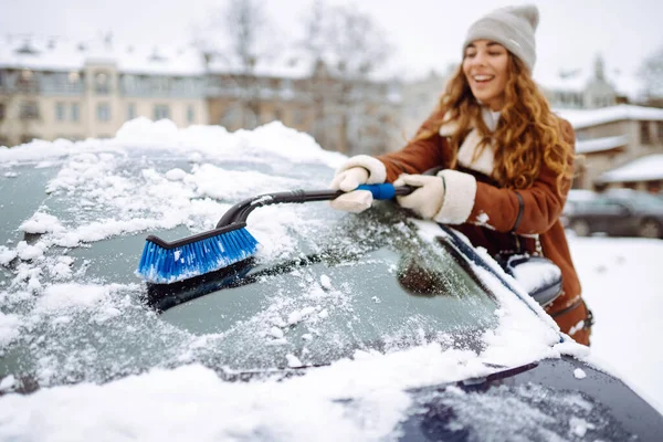 是时候清理雪了 一个年轻的女人用刷子擦去车上的雪 冬季汽车概念 免版税图库图片