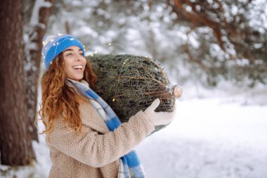 Gülümseyen kadın eve Noel ağacı taşıyor. O, güzel kış havasının tadını çıkarıyor. Kış tatili kavramı, mutluluk, rahatlama..