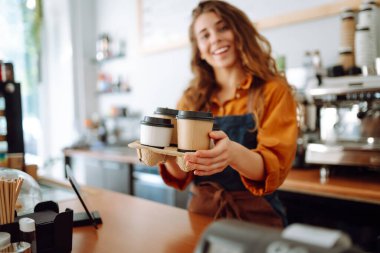 Genç bayan barista elinde tek kullanımlık bardakla sıcak bir içecek tutuyor. Paket teslimat konsepti. Paket yemek kavramı, iş