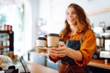 Genç bayan barista elinde tek kullanımlık bardakla sıcak bir içecek tutuyor. Paket teslimat konsepti. Paket yemek kavramı, iş